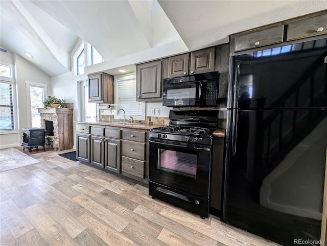 kitchen with dark brown cabinetry, sink, high vaulted ceiling, light hardwood / wood-style floors, and black appliances