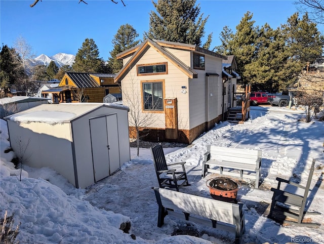 snow covered house featuring a mountain view, a storage shed, and an outdoor fire pit