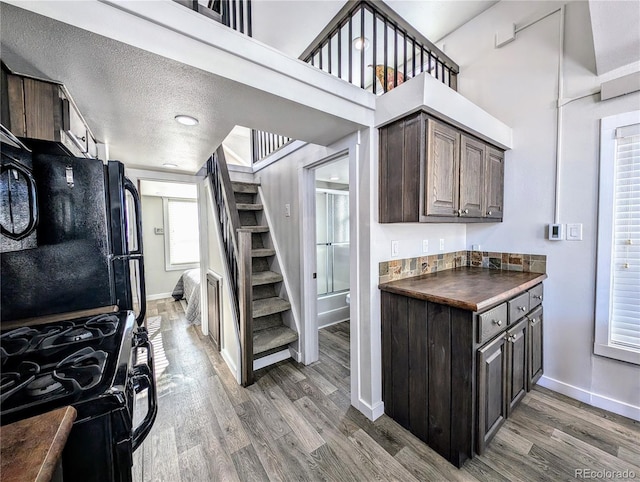 kitchen with black appliances, wood-type flooring, dark brown cabinetry, and a textured ceiling