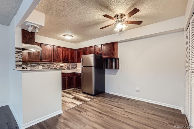 kitchen featuring decorative backsplash, stainless steel fridge, light hardwood / wood-style floors, and a textured ceiling