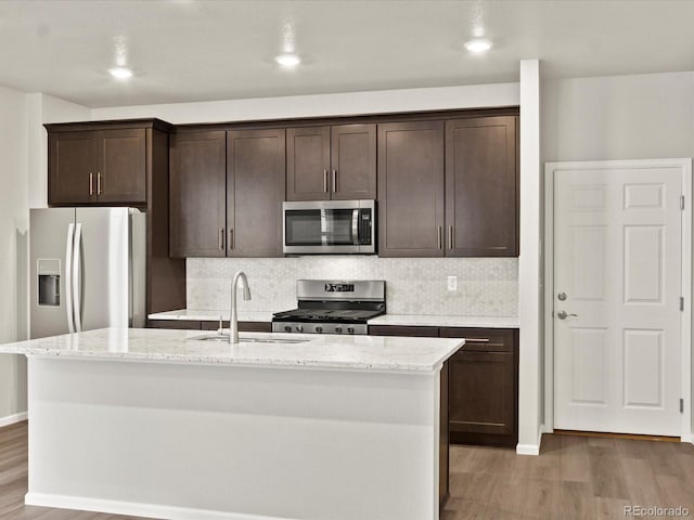 kitchen featuring appliances with stainless steel finishes, sink, light stone countertops, and a center island with sink