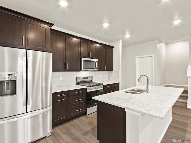 kitchen with light hardwood / wood-style flooring, sink, light stone counters, stainless steel appliances, and a kitchen island with sink