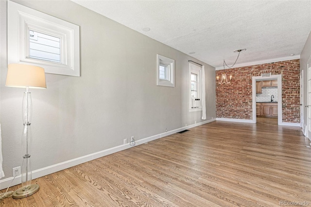 unfurnished living room with a notable chandelier, sink, hardwood / wood-style flooring, a textured ceiling, and brick wall