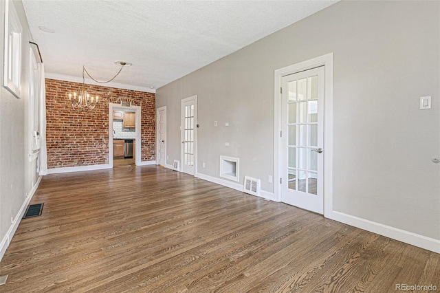 unfurnished living room featuring a fireplace, hardwood / wood-style floors, an inviting chandelier, a textured ceiling, and brick wall