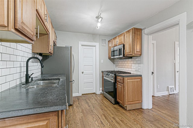 kitchen with appliances with stainless steel finishes, tasteful backsplash, sink, rail lighting, and light hardwood / wood-style flooring