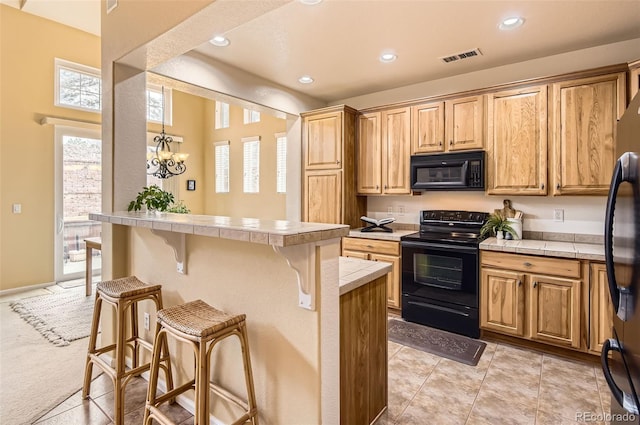 kitchen with black appliances, tile counters, light colored carpet, a breakfast bar area, and a chandelier