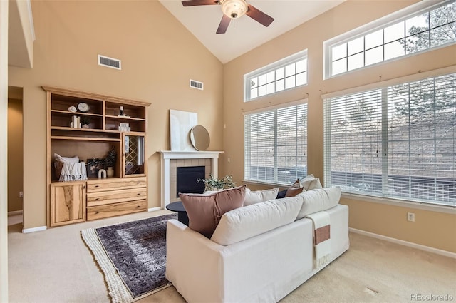 carpeted living room featuring ceiling fan, a fireplace, and a towering ceiling