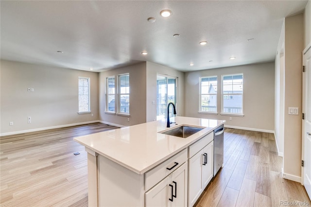 kitchen with light hardwood / wood-style floors, white cabinets, sink, an island with sink, and stainless steel dishwasher