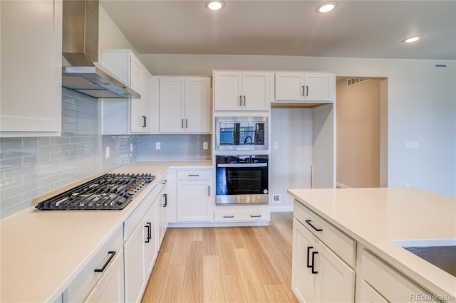 kitchen featuring light wood-type flooring, white cabinets, wall chimney exhaust hood, and stainless steel appliances