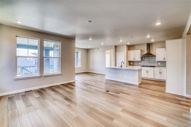 kitchen featuring sink, light hardwood / wood-style floors, white cabinets, wall chimney exhaust hood, and a kitchen island with sink