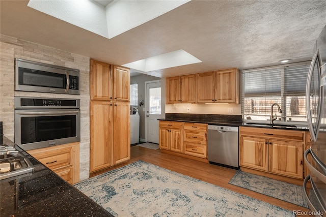 kitchen featuring sink, light hardwood / wood-style flooring, appliances with stainless steel finishes, a textured ceiling, and washer / clothes dryer