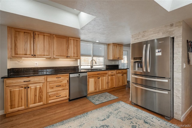 kitchen with sink, dark stone countertops, stainless steel appliances, light hardwood / wood-style floors, and a textured ceiling