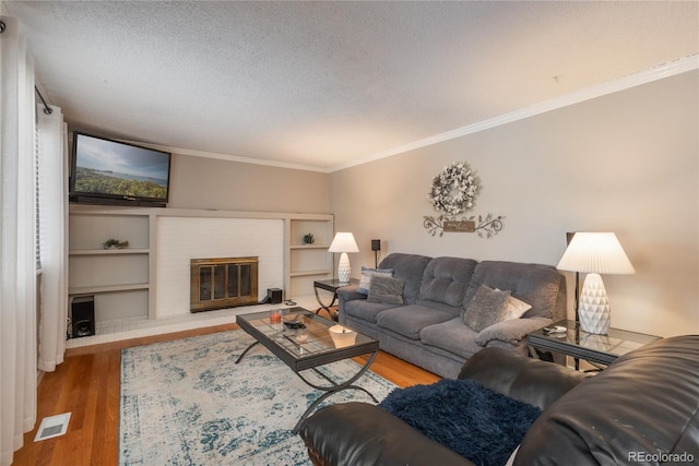 living room with hardwood / wood-style flooring, a fireplace, ornamental molding, and a textured ceiling