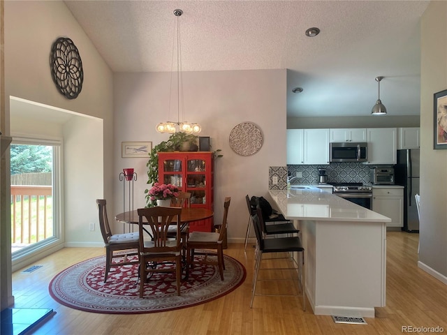 5479 E Weaver Ave, Centennial, CO 80121 - dining space with light wood finished floors, a textured ceiling, high vaulted ceiling, and a chandelier