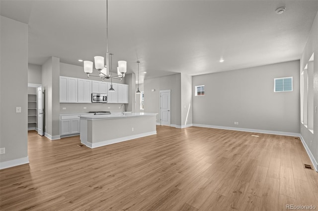 21034 E 63rd Dr, Aurora, CO 80019 - kitchen with stainless steel microwave, a chandelier, open floor plan, light wood-style floors, and white cabinetry