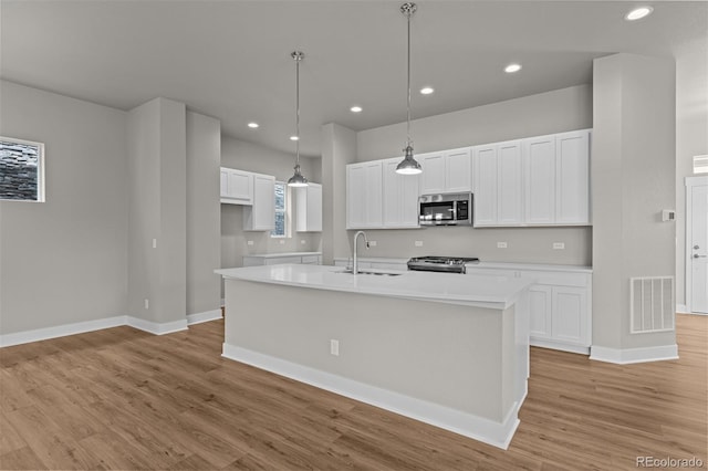 21034 E 63rd Dr, Aurora, CO 80019 - kitchen with appliances with stainless steel finishes, light wood-type flooring, a center island with sink, white cabinetry, and recessed lighting