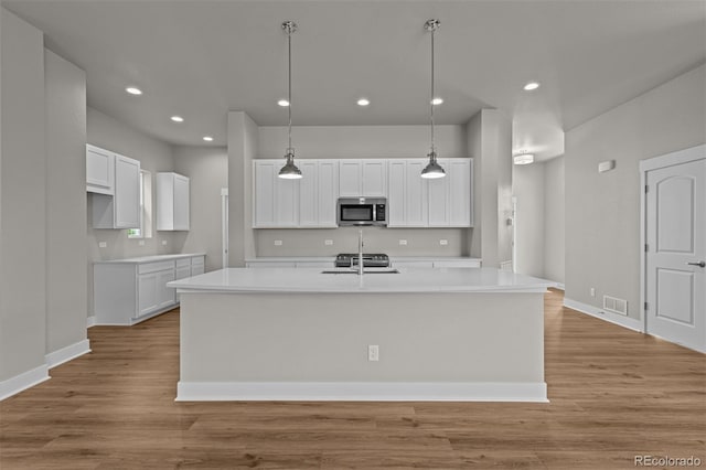 21034 E 63rd Dr, Aurora, CO 80019 - kitchen featuring stainless steel microwave, white cabinetry, an island with sink, light wood-style flooring, and light countertops