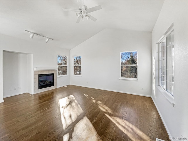 unfurnished living room with lofted ceiling, dark wood-type flooring, track lighting, ceiling fan, and a tiled fireplace