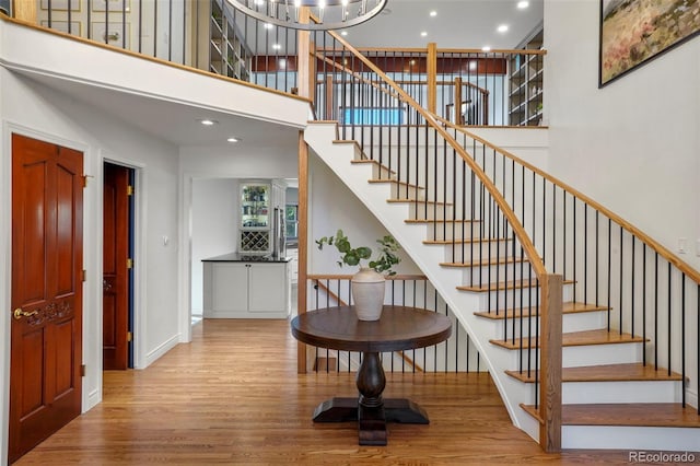 stairs with a high ceiling, wood-type flooring, and an inviting chandelier