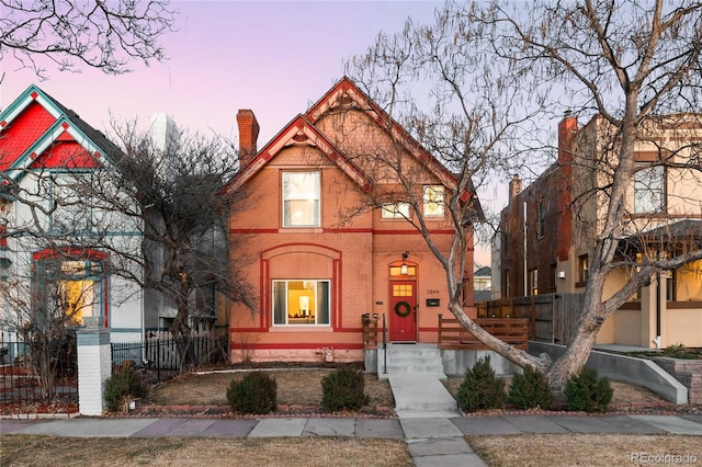 view of front of home with a chimney, fence, and brick siding