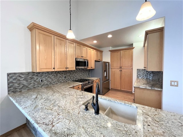 kitchen with appliances with stainless steel finishes, light stone counters, hanging light fixtures, a sink, and backsplash