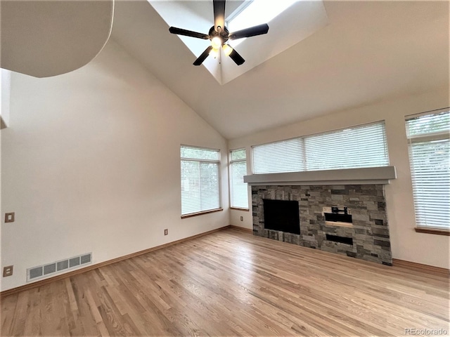 unfurnished living room with a ceiling fan, visible vents, a stone fireplace, and light wood finished floors