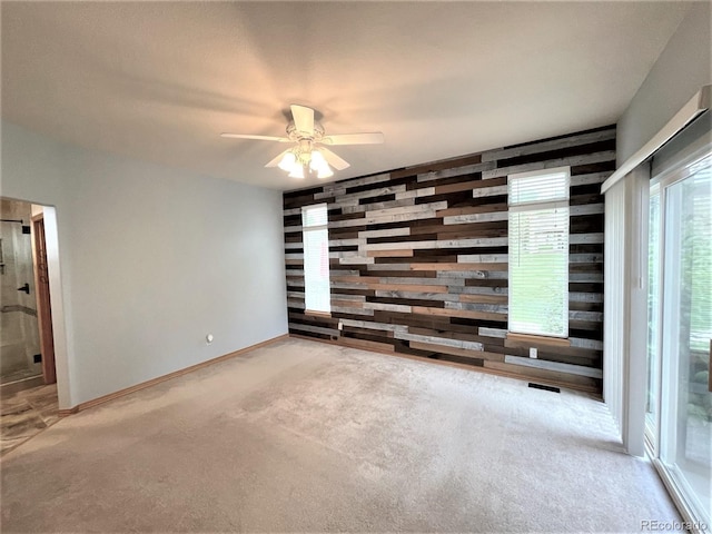 carpeted spare room featuring ceiling fan, an accent wall, wood walls, and baseboards