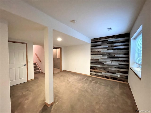 below grade area featuring visible vents, an accent wall, stairs, carpet floors, and wood walls