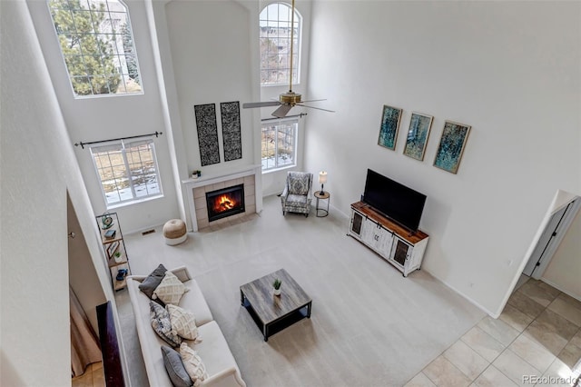 living area with tile patterned flooring, visible vents, ceiling fan, a tiled fireplace, and a high ceiling