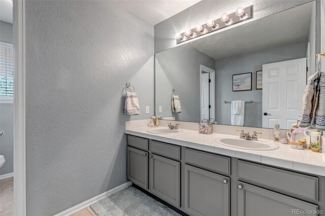 full bathroom with double vanity, a textured wall, and a sink