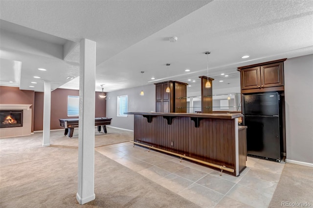 kitchen with a glass covered fireplace, a breakfast bar area, freestanding refrigerator, and light carpet