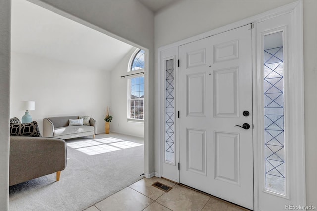 carpeted foyer featuring tile patterned flooring, visible vents, and lofted ceiling