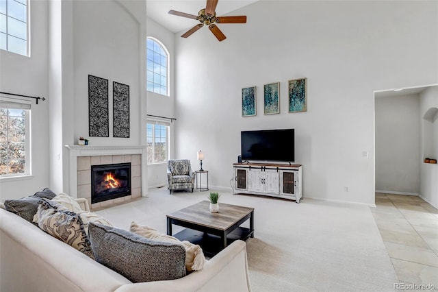 carpeted living area featuring baseboards, a high ceiling, a fireplace, ceiling fan, and tile patterned floors