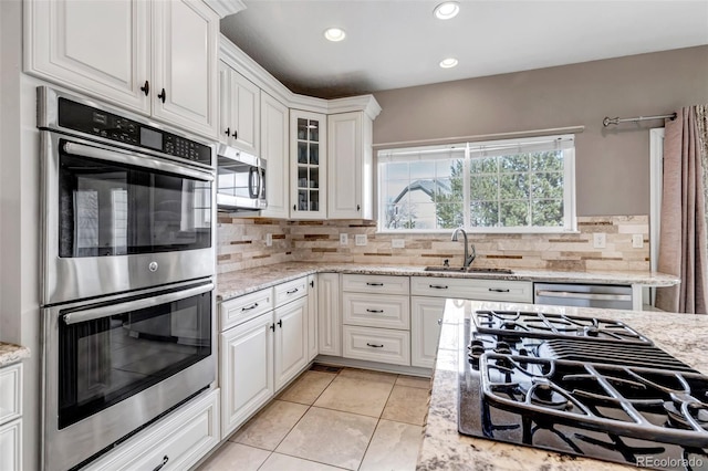 kitchen with a sink, decorative backsplash, stainless steel appliances, white cabinets, and glass insert cabinets