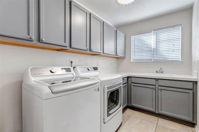 washroom with cabinet space, light tile patterned floors, washing machine and dryer, and a sink