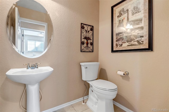 half bathroom featuring tile patterned flooring, toilet, baseboards, and a sink