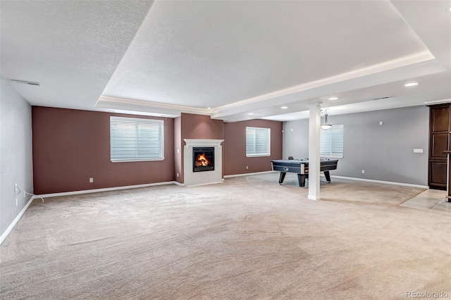 unfurnished living room featuring baseboards, a tray ceiling, a textured ceiling, a glass covered fireplace, and light colored carpet