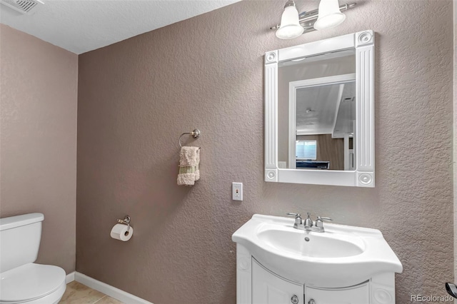 bathroom featuring visible vents, toilet, vanity, and a textured wall