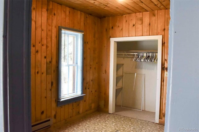 unfurnished bedroom featuring a closet, baseboard heating, wooden walls, and multiple windows