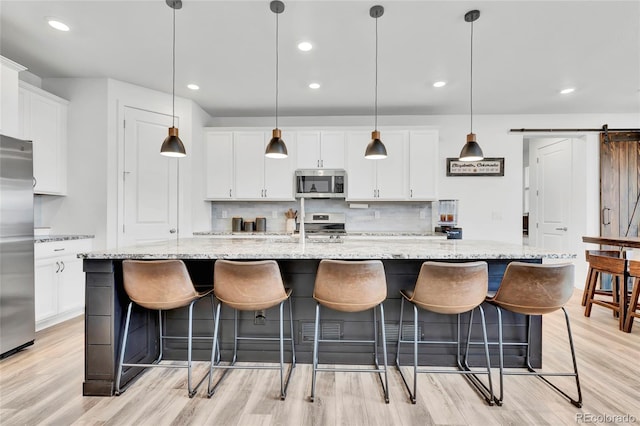 kitchen with a barn door, a large island, pendant lighting, and appliances with stainless steel finishes