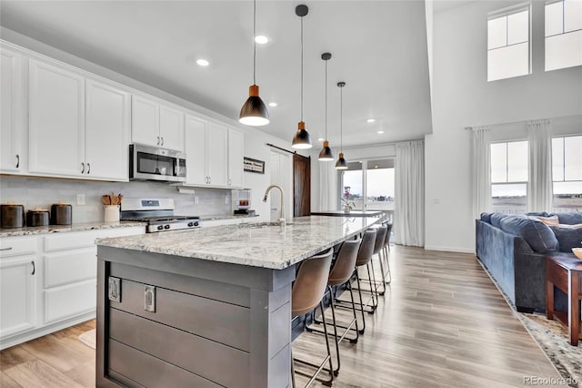 kitchen with range, a center island with sink, a kitchen breakfast bar, sink, and white cabinetry