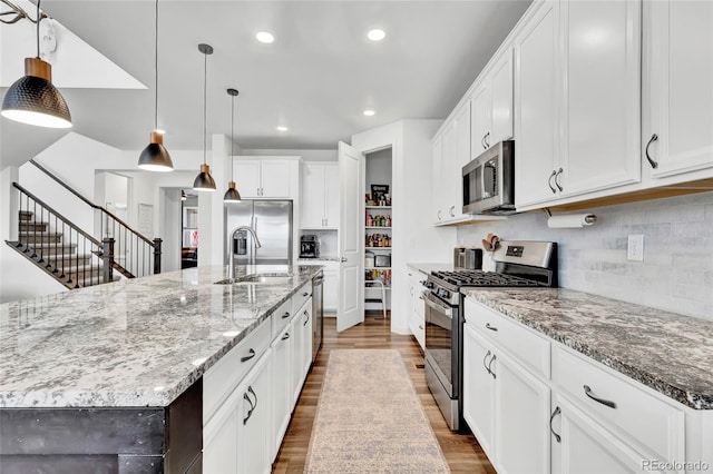 kitchen with a large island with sink, stainless steel appliances, white cabinetry, and decorative light fixtures