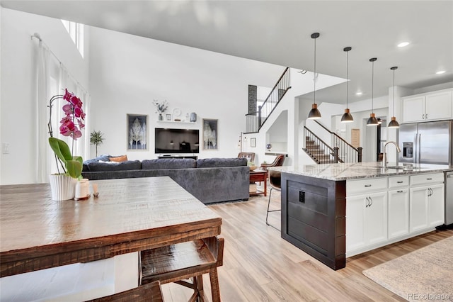 kitchen featuring light stone counters, a kitchen island with sink, pendant lighting, light hardwood / wood-style flooring, and white cabinetry