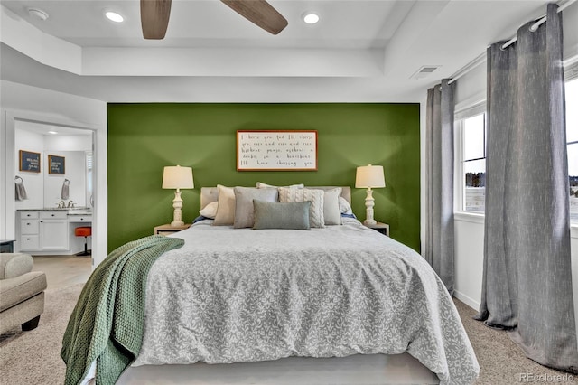 carpeted bedroom featuring connected bathroom, a tray ceiling, and ceiling fan