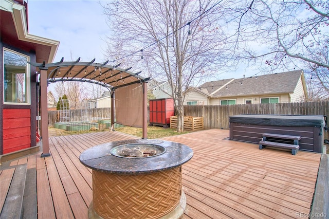 wooden terrace featuring a fire pit, a hot tub, and a storage unit