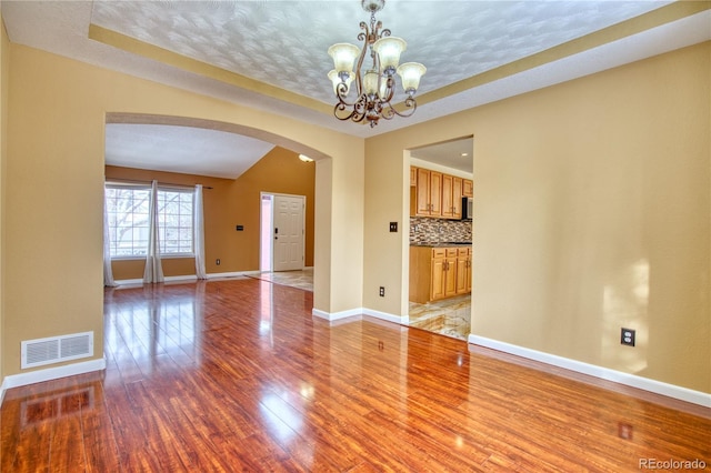 empty room with a textured ceiling, a notable chandelier, light hardwood / wood-style flooring, and a tray ceiling