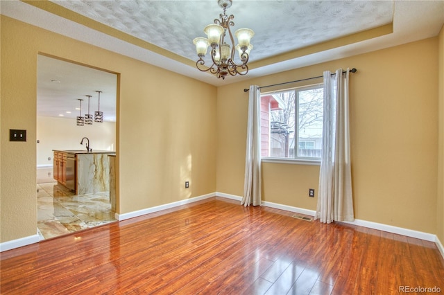 spare room with a raised ceiling, sink, a textured ceiling, wood-type flooring, and a chandelier