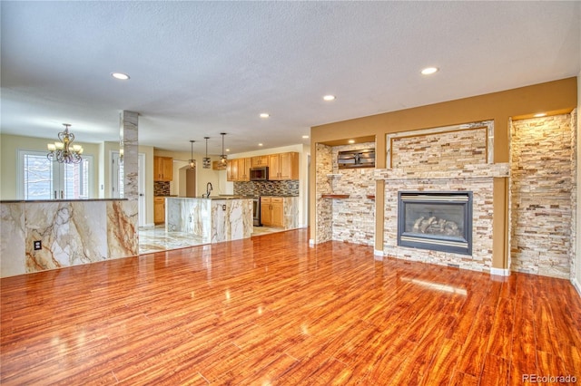 unfurnished living room featuring light wood-type flooring, a textured ceiling, sink, a chandelier, and a stone fireplace