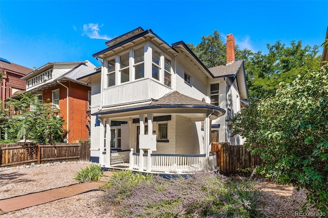 view of front facade with covered porch, brick siding, a chimney, and fence