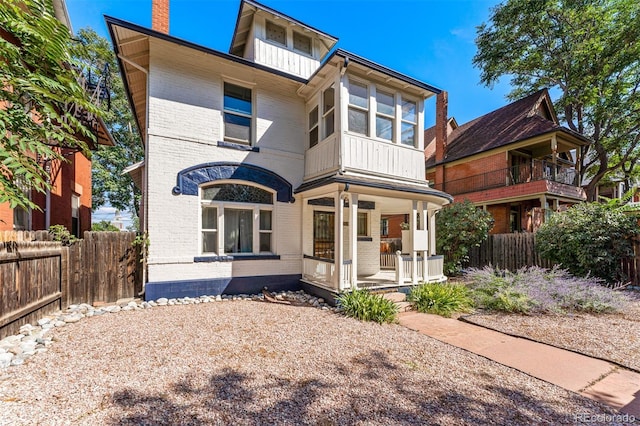 view of front of property with covered porch, brick siding, fence, and a chimney